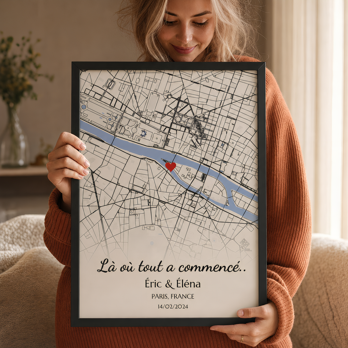 Femme tenant l'affiche lieu de rencontre personnalisée encadrée : carte de Paris, cœur rouge, prénoms et date